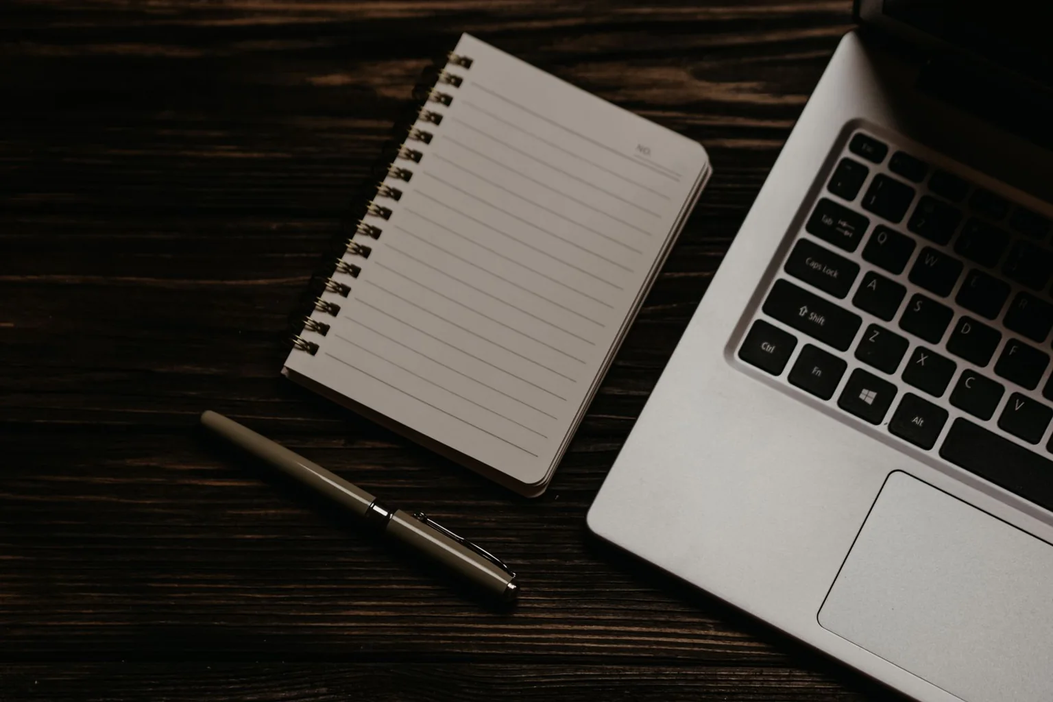 Laptop, notebook and pen on a dark wooden desk